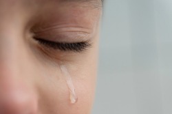 Close up image of teardrop rolls down the boy's cheek, his eyes are closed, he is upset and crying. Sad, unhappy emotions of child.