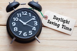Daylight Saving Time words written on tag label with clock on wood background,Conceptual