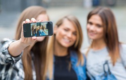 Best friends. Young friends girls are having fun together on the street and smile at each other. Funny and beautiful friends are doing selfie on cell phone