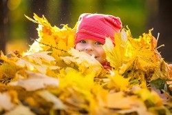 Little girl playing with autumn leaves in the park