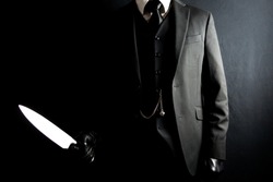Portrait of Man in Dark Suit and Leather Gloves Holding Sharp Knife on Black Background. Well Dressed Gentleman Killer. Mafia Hit Man in Stylish Suit.