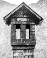 Old traditional chimney in the shape of a small house with roof and windows. Unusually shaped  chimney with multiple openings and a roof.