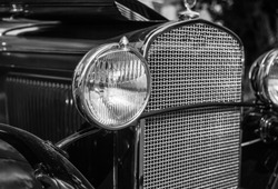 Headlight and grill of vintage automobile in black and white.