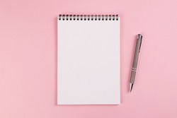 A notebook with a blank page and a ballpoint pen lie on a pink background. Copy space, layout, mockup.