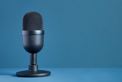 Minimalist image of a modern and elegant black design microphone for streaming and gaming on a colorful blue background with texture and copy space. Technology and entertainment.