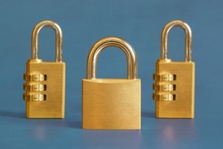 A golden square padlock escorted by two rectangular combination padlocks s in the background on a blue-painted study table. Leadership and security concept.
