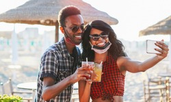 African american couple taking selfie in beach party - Young friends with face mask drinking cocktail in holiday - Coronavirus summer 2020
