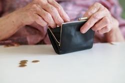A wallet in the hands of an old woman, a grandmother puts and counts coins in her empty leather wallet, poverty and misery of the older generation, wrinkled hands close-up.
