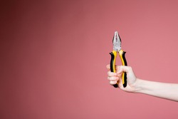 Female hand on a pink background in the studio holds pliers as an advertising banner for a construction store and services.