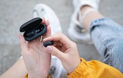 close-up of a woman taking out a black wireless earbud from his charging box. Female hands touching a portable gadget headphones