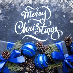 Merry Christmas hand lettering. Christmas gift with blue ribbon and blue balls, tree branches and cones on dark blue background.