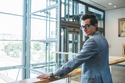 Serious formal dressed male in eyeglasses looking over shoulder while standing in office space of well lit modern stylish office building
