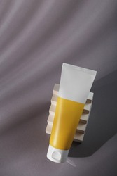 White orange mockup tube on grey background in harsh light with white concrete decor. Mineral conditioner template, sunscreen cream, balm or body lotion. No brand