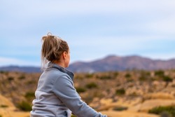 Woman tourist seen in Joshua Tree National Park waiting for sunset views over the desert landscape. 