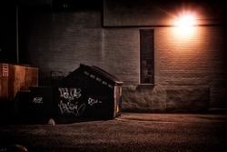 A dirty, dark, shadowy and dangerous looking urban back-alley at night time with garbage dumpster.