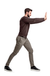 A bearded man in casual clothes tries to push a heavy object with both arms with one leg put in front for balance. Physical force. Test of strength. Man at work.