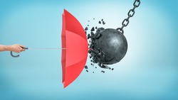 A male hand holding an open red umbrella which protects from a collision with a broken wrecking ball. Insurance and protection. Safety measures. IT defense.