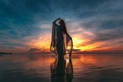 silhouette of young fashionable woman standing in water on the beach at sunset