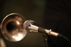 A shiny microphone in front of the blurry bell of a nightclub player's brass trumpet instrument.Art photography.Musical background.Close-up