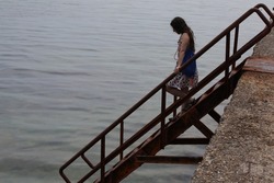 View of a woman descending the iron stairs with rusty steps to the sea from the pier