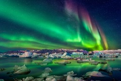 Fantastic Aurora borealis over the sea and snowy mountains at night. Northern lights with glaciers and reflection in water on foreground. Starry sky with polar lights. Winter ice landscape with Aurora