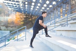 young asian runner athlete with muscle pain. Man massaging Stretching, trauma injury while jogging at the stadium outdoors. Fitness male sprain severe pain stretch pull. Leg muscle cramp calf sport