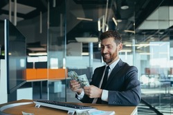 Joyful business man in sitting at desk working on laptop computer in bright office Achieving business career concept. Keep cash by making a gesture to the winner