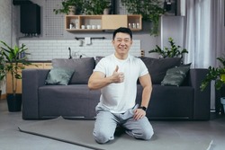 Portrait of a happy Asian man doing fitness and doing morning exercises in the morning, man sitting on a sports mat and looking at the camera motivated