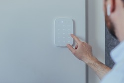 Businessman enters finger password lock code on alarm panel, on white wall, rear view of man with beard