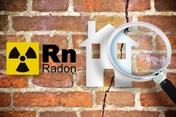 The danger of radon gas in our homes - concept with periodic table of the elements, radioactive warning symbol and home silhouette seen through a magnifying glass against a cracked brick wal