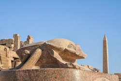 Statue of Khepri the sacred scarab in Karnak Temple Complex (Luxor, Egypt) with obelisk and blue sky in background