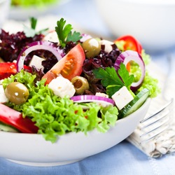 Greek salad with juicy tomatoes, feta cheese,  lettuce, green olives, cucumber, red onion and fresh parsley. Homemade food. Symbolic image. Concept for a tasty and healthy vegetarian meal. Close up. 