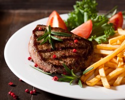 Grilled beef steak with french fries, tomatoes, lettuce and fresh rosemary. Home made food. Concept for a tasty and hearty meal.  Rustic wooden background. Close up.