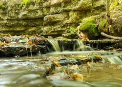 a small rapid river flows through dolomite rocks, long-term exposure, gentle and fuzzy river water, colorful autumn leaves and dry branches in the river