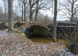landscape with a continuous boulder stone bridge with a brick used for masonry, early spring, bare trees, snow plan on the ground, Stone arch bridge over the river Kuja, Madona, Latvia
