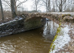 landscape with a continuous boulder stone bridge with a brick used for masonry, early spring, bare trees, snow plan on the ground, Stone arch bridge over the river Kuja, Madona, Latvia