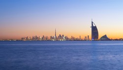 Dubai, UAE - 03/30/2020 : Burj Al Arab in Jumeirah Island or boat building with waves on sea beach, Downtown skyline. Financial district in urban city. Skyscrapers at sunset.