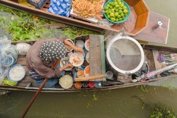 Market woman cooking noodle at Damnoen Saduak Floating Market or Amphawa. Local people sell fruits, traditional food on boats in canal, Ratchaburi District, Thailand. Famous Asian tourist attraction.