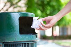 Closeup cropped portrait of someone tossing crumpled piece of paper in trash can, isolated outdoors green trees background