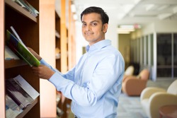 Closeup portrait, young business man in blue shirt reading, perusing books, magazines, and periodicals at library