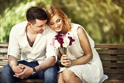 Young attractive couple sitting on bench in the park and romantic smiling.