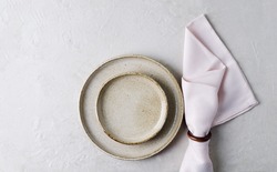 Beige ceramic plates and a pink napkin on a beige stone table. Top view, copy of space. Table setting, menu background, layout, recipe background, food flat layout