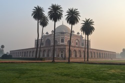 Bunch of palm trees and mesmerizing view of humayun tomb memorial from the side of the lawn at winter foggy morning.