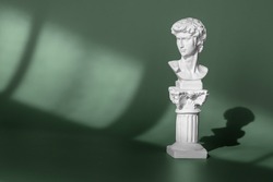 White marble head of young man, head of famous statue by Michelangelo - David from Florence. Gypsum copy of ancient statue head on green background with light and shadow