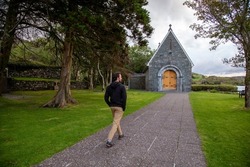 A man walking  towards a church at Gougane Barra National Park, Ireland