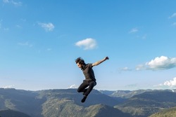 Young man dressed in black clothes jumping on a mountains and blue sky background, in Nova Petropolis, Rio Grande do Sul sierra, Brazil