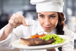 Professional female chef in a hat makes final touches on a freshly made steak before serving.
