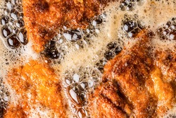 Detail of schnitzels in breadcrumbs sizzling in frying oil.