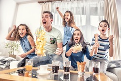 Raving fans cheering sports, as family of five watch football, or ice-hockey match on the TV at home, screaming from joy.