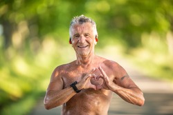Old but fit man with grey hair shows a heart gesture with his fingers as a sign of his healthy cardiovascular system.